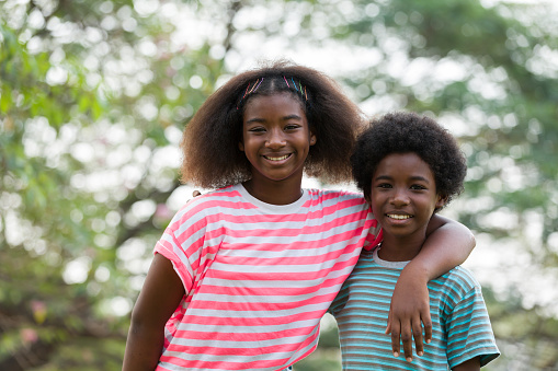 Smiling African American boy and girl playing and hugging together outdoor. Happy afro kid having fun or enjoying together in the park. Happy black people. Education and field trips concept
